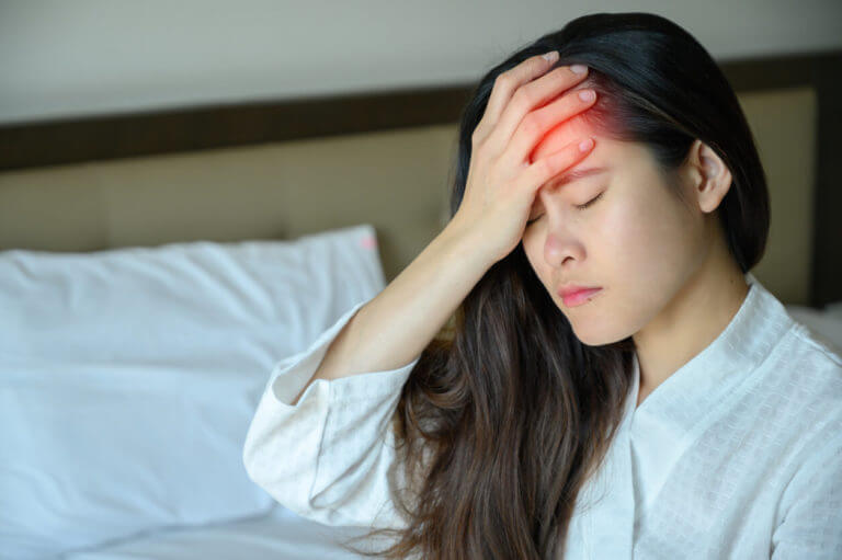 Image of a young Asian woman sitting on a bed and suffering from Severe headaches.